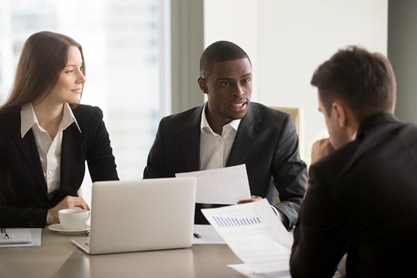 three people in business attire negotiating a contract at a desk